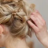 Eine Hand formt mittellange hochgesteckte Haare zu einem kunstvollen Zopf.