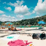 Gente disfrutando de unas **vacaciones agosto 2026** en una playa tropical, con aguas turquesas y vegetación exuberante.