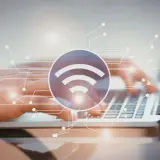Dłonie piszące na laptopie, symbol Wi-Fi i schemat połączeń. Dowiedz się, jak sprawdzić pasmo Wi-Fi w telefonie.