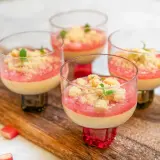 Fyra glas med krämig pannacotta med rabarberkompott och smuldeg. Garnerad med mynta. En härlig sommardessert.