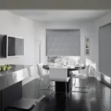 Tende antirumore funzionano: un elegante soggiorno con tavolo da pranzo apparecchiato e tende a rullo con motivo floreale che bloccano il rumore esterno.