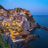 Village coloré accroché à la falaise, au crépuscule, dans le site de Cinque Terre. Bateaux dans le port, mer bleue.