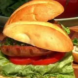 Sandwich de salchicha con lechuga, tomate y salsa chimichurri, con sus ingredientes frescos listos para servir.