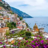 Colorful buildings cascade down a cliffside along the Amalfi road, overlooking a sparkling blue sea dotted with boats.