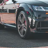 Zbliżenie na czarne, sportowe auto z widoczną felgą i oponą.