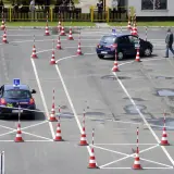 Plac manewrowy kat B. Dwa samochody z literą L na dachu i pachołki wyznaczają trasę egzaminu na prawo jazdy.