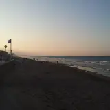Gente pasea por la **playa de Piles** al atardecer, con el mar y el cielo en tonos pastel.