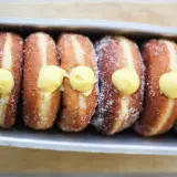 Una fila di bomboloni alla crema, cosparsi di zucchero, pronti per essere gustati.