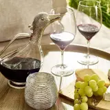 Dekantiert bedeutet, Wein in eine Karaffe zu füllen, um ihn zu belüften. Hier: ein Entenkaraffe mit Rotwein, Gläser, Käse und Trauben.