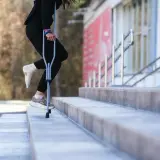 Osoba z zabandażowaną stopą uczy się, jak chodzić o kulach, pokonując schody.