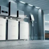 Nowoczesny magazyn energii off grid z bateriami litowo-jonowymi i ładowarką. W tle panele słoneczne i turbiny wiatrowe.