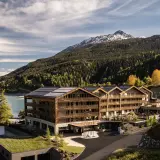 Das Gerstl Family Retreat, un hotel moderno con pannelli solari, si affaccia su un lago alpino e montagne boscose.