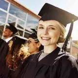 Uśmiechnięta absolwentka w togach i birecie, obok innych studentów. To symbol końca nauki i wyboru nowych kierunków liceum.