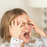 Mała dziewczynka z rękami na twarzy, krzycząca w wyrazie frustracji, być może objaw zaburzeń opozycyjno buntowniczych.
