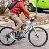 Enjoying the benefits of electric bikes: a person rides a sleek e-bike past a green Jeep, showcasing an eco-friendly commute.