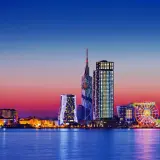 Widok na nowoczesną panoramę Batumi, stolicę Adżarii, o zachodzie słońca. Błyszczące wieżowce i diabelski młyn odbijają się w spokojnej wodzie.