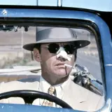Jack Nicholson w kapeluszu i okularach przeciwsłonecznych, z plastrem na nosie, pali papierosa za kierownicą kabrioletu. Scena z filmu Polańskiego z Nicholsonem.