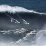 Surferzy ścigają się po gigantycznych nazare falach, tworząc białe smugi na ciemnym oceanie.