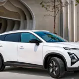 Biały OMODA hybryda zaparkowany przed nowoczesnym budynkiem. Stylowy SUV z charakterystycznym grillem i dynamiczną linią nadwozia.