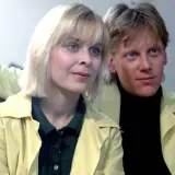 W labiryncie obsada: blondynka i blondyn w żółtych płaszczach, siedzą obok siebie.