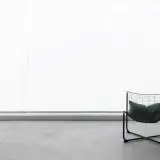 Nowoczesne wnętrze z betonową kolumną i minimalistycznym fotelem. Na ścianie widoczny jest efekt mikrocementu, nadający surowy, industrialny charakter.