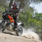 Motociclista con casco y equipo de aventura, derrapando una KTM 490 Adventure en un camino de tierra con polvo levantándose.