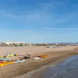 Gente prepara kayaks y tablas en la playa Malvarrosa, lista para un día de sol y mar.