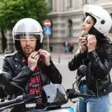 Coppia in moto, lui sistema il suo casco nuovo che fa male, lei il suo.