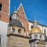 Katedra Wawelska z bliska: ceglana wieża, złota i czarne kopuły, detale architektoniczne.