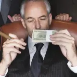 Mężczyzna w garniturze z cygarem w dłoni wącha stos banknotów. Sekret jak że 100 tys zrobić milion?