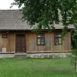 Drewniany dom z gontowym dachem, otoczony zielenią. Widać tu, kiedy dom jest zabytkiem, z jego wiekową, ale wciąż piękną fasadą.