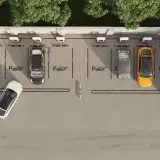 Widok z góry na parking z kilkoma samochodami, w tym żółtym i białym. Widać ładowarki do samochodów elektrycznych, sugerujące funkcję asystenta parkowania.