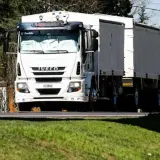 Biała ciężarówka Iveco z naczepą jedzie drogą. Kierowca ciężarówek wyrusza w długą trasę.