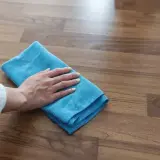 Mano con panno blu pulisce pavimento in gres effetto legno. Scopri come togliere la colla dal pavimento in gres con metodi efficaci.