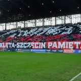 Trybuna stadionu podczas meczu Pogoń Szczecin – Widzew Łódź. Kibice tworzą biało-czerwony transparent "ARMIO WYKLETA-SZCZECIN PAMIĘTA!".