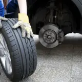 Osoba w rękawicach trzyma nową oponę, zastanawiając się, czy lepsze opony na przód czy tył zapewnią lepszą przyczepność.