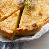 Delizioso gateau di patate dorato e croccante, guarnito con rosmarino fresco. Una fetta è già stata tagliata, invitando ad assaporare questo piatto.