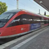Roter Zug der euregiobahn br 643 steht am Bahnsteig. Grüne Bäume und blauer Himmel im Hintergrund.