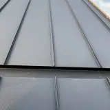 Szara blacha na rąbek stojący z widocznymi wadami montażu, np. szczeliną i uszkodzeniem przy okapie.