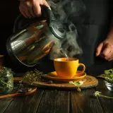 Heißer Kräutertee wird in eine gelbe Tasse gegossen. Ein Hausmittel gegen körperliche Erschöpfung, zubereitet aus getrockneten Kräutern.