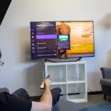 Mężczyzna w fotelu ogląda telewizor z menu ustawień, gdzie widać słonia. To moment, kiedy telewizor pobiera najwięcej prądu.