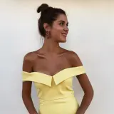 Mujer con moño alto y pendientes rojos, luciendo un vestido amarillo de hombros caídos. Ideas para combinar zapatos para vestido amarillo.