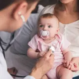 Un médecin examine un bébé avec un stéthoscope, vérifiant les symptômes de la coqueluche.