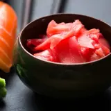 Miseczka z różowym, marynowanym imbirem obok sushi i wasabi. Idealny dodatek do japońskich przysmaków.