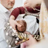 Woda święcona spływa na główkę niemowlęcia, rozpoczynając uroczysty obrzęd chrztu.
