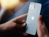 Dłonie trzymające szare iPhone'a z widocznym logo Apple i modułem aparatów.