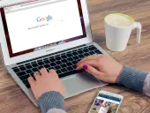 Kobieta pisze na laptopie z otwartą wyszukiwarką Google, obok stoi kubek kawy i smartfon.