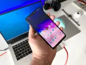 Dłoń trzyma smartfon podłączony kablem do laptopa.