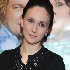 Ilona Ostrowska, znana z wielu filmów, pozuje z uśmiechem. W tle plakaty z innymi aktorami.