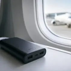 Czarny powerbank w bagażu podręcznym na stoliku w samolocie, gotowy do ładowania urządzeń podczas lotu.